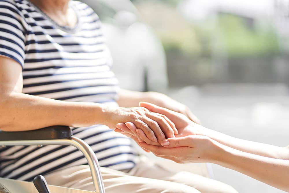 Younger woman holding the hand of a woman in a wheelchair